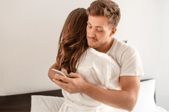 man hugging his wife while texting to a woman